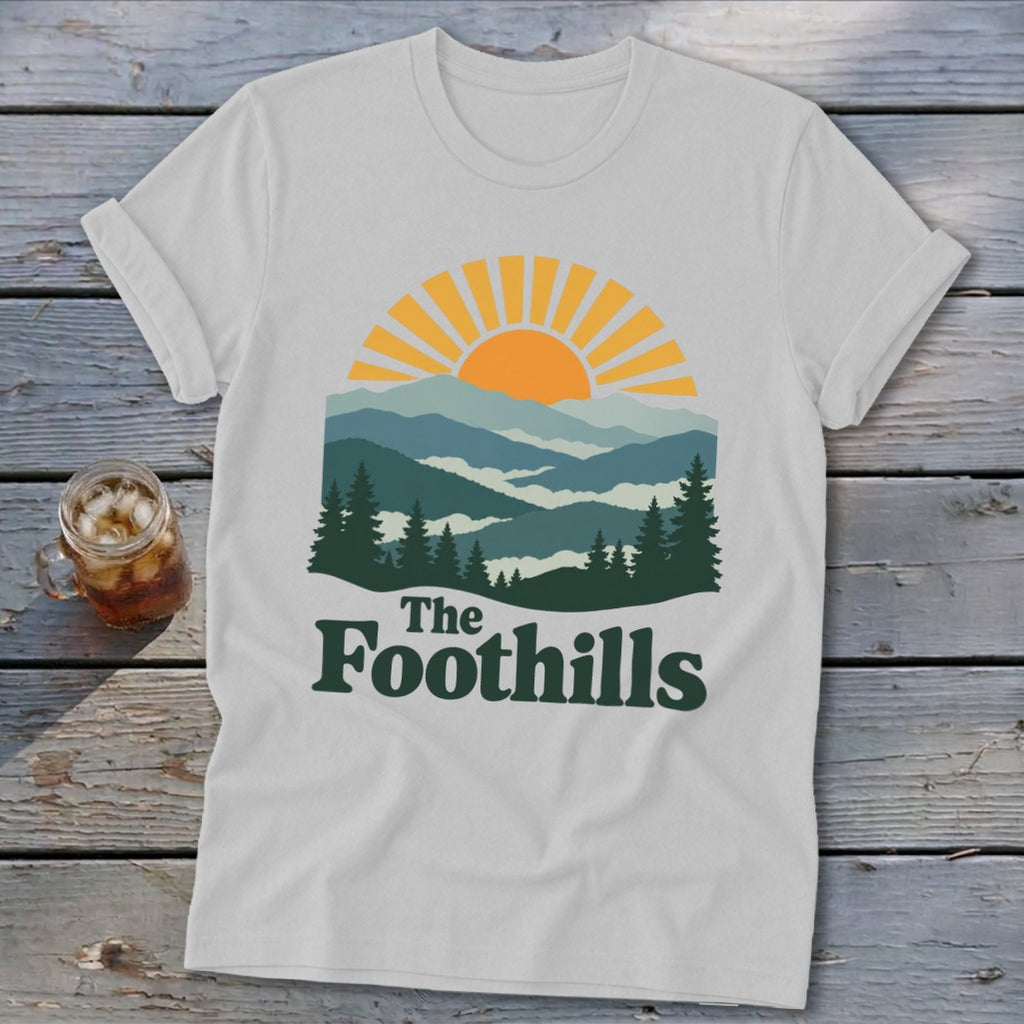 White t-shirt with "The Foothills" text and mountain sunset graphic.