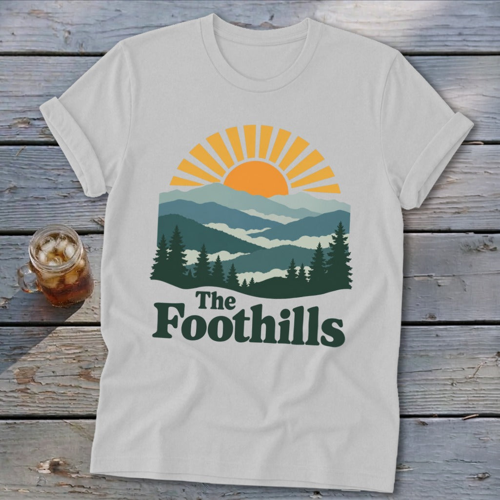 White t-shirt with "The Foothills" text and mountain sunset graphic.