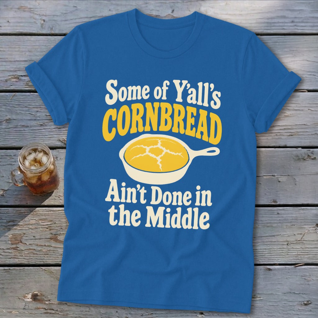A blue crewneck t-shirt features text that reads, Some of Y'all's Cornbread Ain't Done in the Middle, alongside a cast-iron skillet illustration.