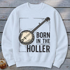 White sweatshirt with a black banjo illustration and text that reads "BORN IN THE HOLLER".