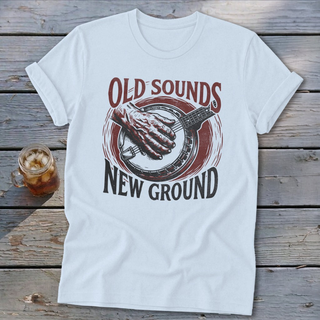 A white t-shirt featuring a retro graphic of a hand playing a banjo with the text "Old Sounds New Ground."