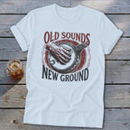 A white t-shirt featuring a retro graphic of a hand playing a banjo with the text "Old Sounds New Ground."