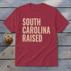Maroon t-shirt with tan text that says "SOUTH CAROLINA RAISED."