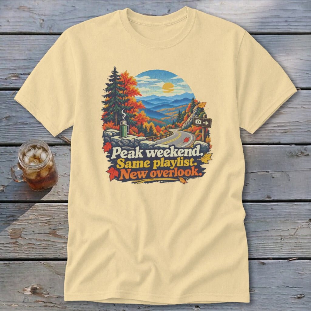 Cream t-shirt with scenic mountain road graphic and text "Peak weekend. Same playlist. New overlook."