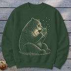 Bear holding a jar of fireflies with grass detail on a green sweatshirt.
