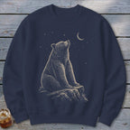 Bear sitting on rock under crescent moon and stars illustration on navy blue sweatshirt.