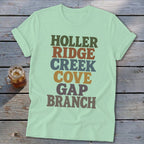 A light green t-shirt with multi-colored stacked text reading Holler Ridge Creek Cove Gap Branch.