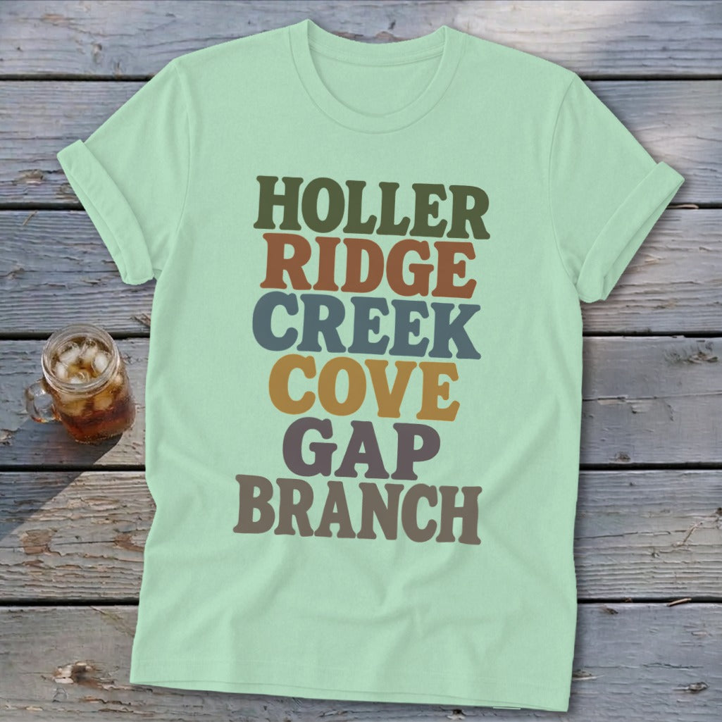 A light green t-shirt with multi-colored stacked text reading Holler Ridge Creek Cove Gap Branch.