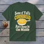 Dark green t-shirt featuring yellow and white text that reads Some of Y'all's Cornbread Ain't Done in the Middle above a skillet of cornbread.