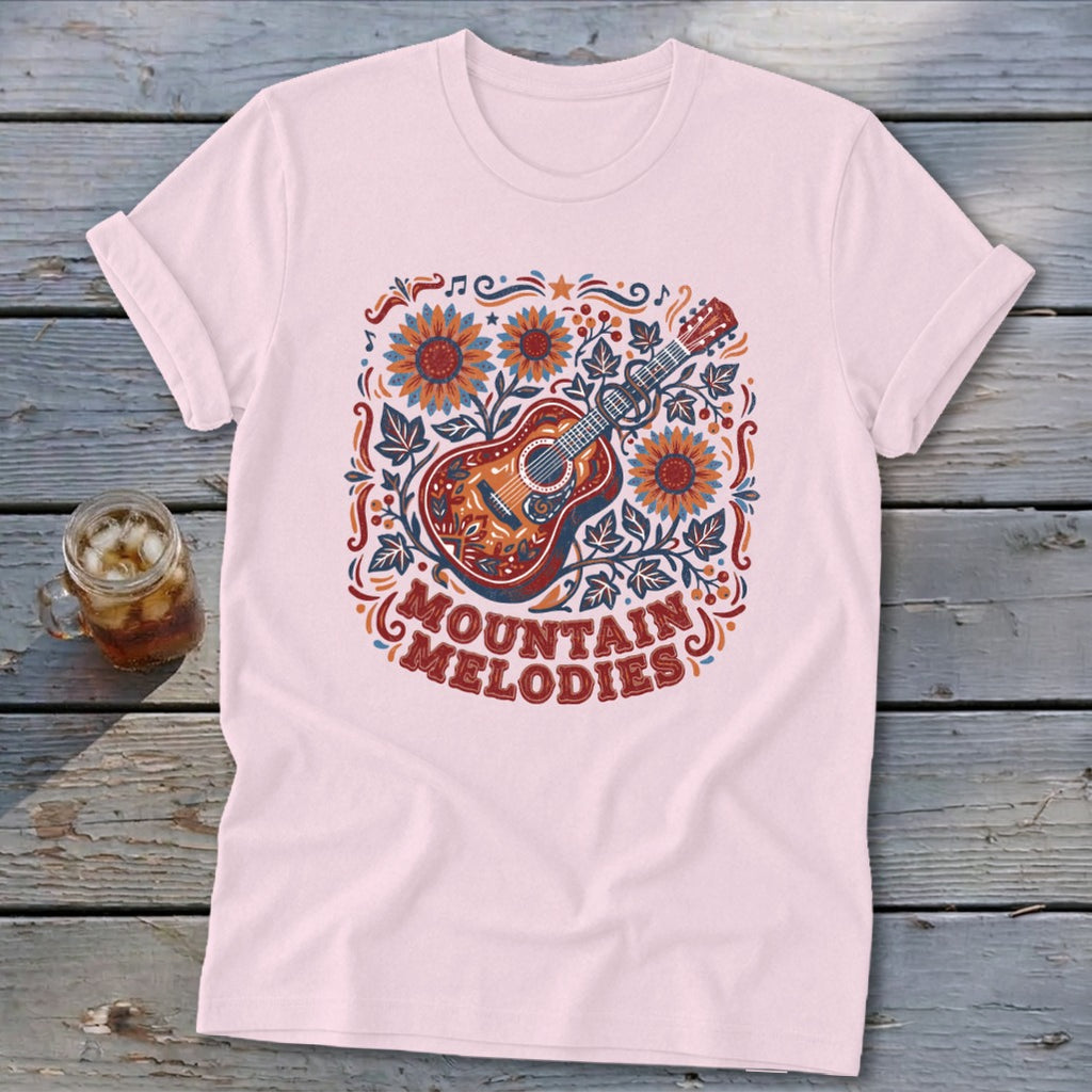 Light pink t-shirt featuring a folk-art acoustic guitar graphic with sunflowers and the text Mountain Melodies.