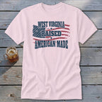Light pink t-shirt featuring a distressed American flag design and text reading West Virginia Raised American Made.