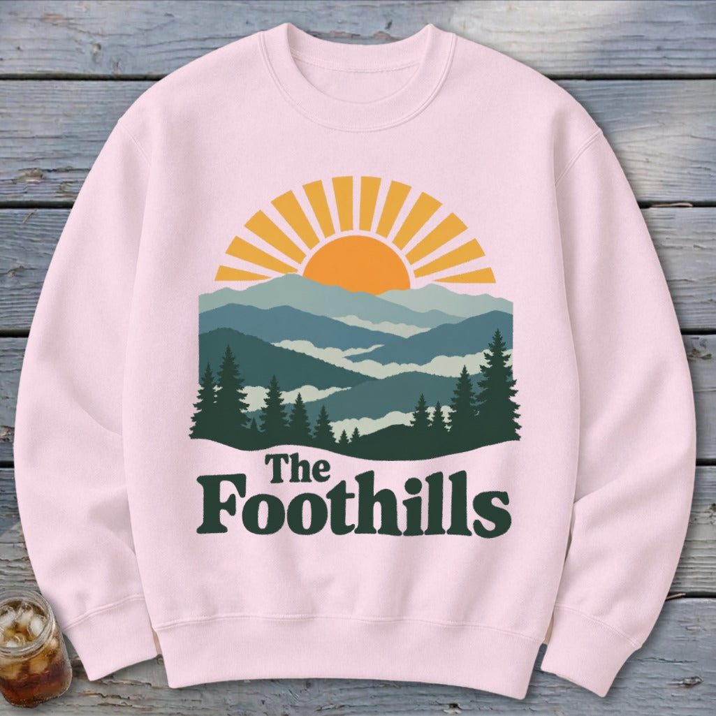 Pink sweatshirt with "The Foothills" text and mountain sunset graphic.