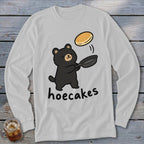 Light gray long-sleeve t-shirt featuring a cartoon black bear flipping a pancake in a pan, with the text hoecakes.