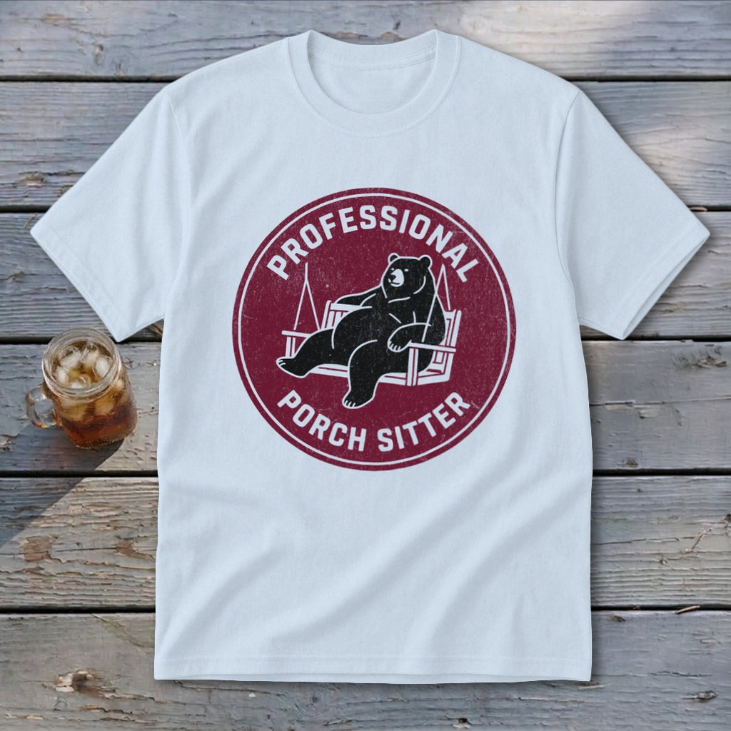 A white short-sleeve t-shirt with a maroon circular graphic of a bear lounging on a porch swing, accompanied by the text "PROFESSIONAL PORCH SITTER".