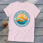 Light pink short-sleeve t-shirt featuring a circular graphic with mountains, a rising sun, and text.