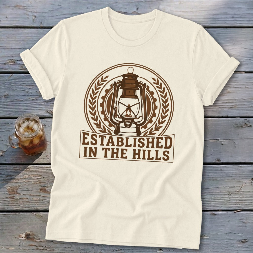 Cream t-shirt with a brown emblem featuring a lantern, gears, and laurel leaves above text.