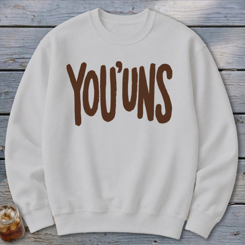 White crewneck sweatshirt with brown "YOU'UNS" text graphic.