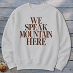 White crewneck sweatshirt with brown text reading "WE SPEAK MOUNTAIN HERE."