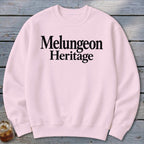 A light pink crewneck sweatshirt with the words Melungeon Heritage printed in bold black lettering across the chest.