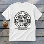 A white t-shirt featuring a circular graphic with text reading Certified Cornbread Judge and a cornbread illustration.
