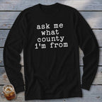 Black long-sleeve t-shirt with white text that reads "ask me what county i'm from".