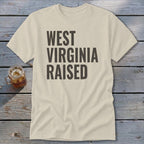 Light tan t-shirt with dark gray text reading "WEST VIRGINIA RAISED".