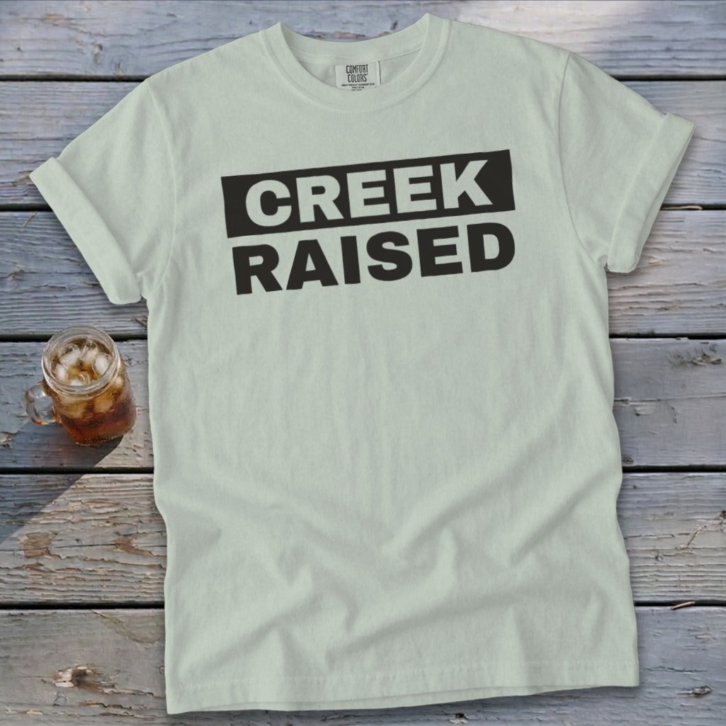 Light green t-shirt with black text that reads "CREEK RAISED".