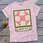 Pink t-shirt with a quilted "Shoo Fly" graphic featuring pink and white squares and floral accents.