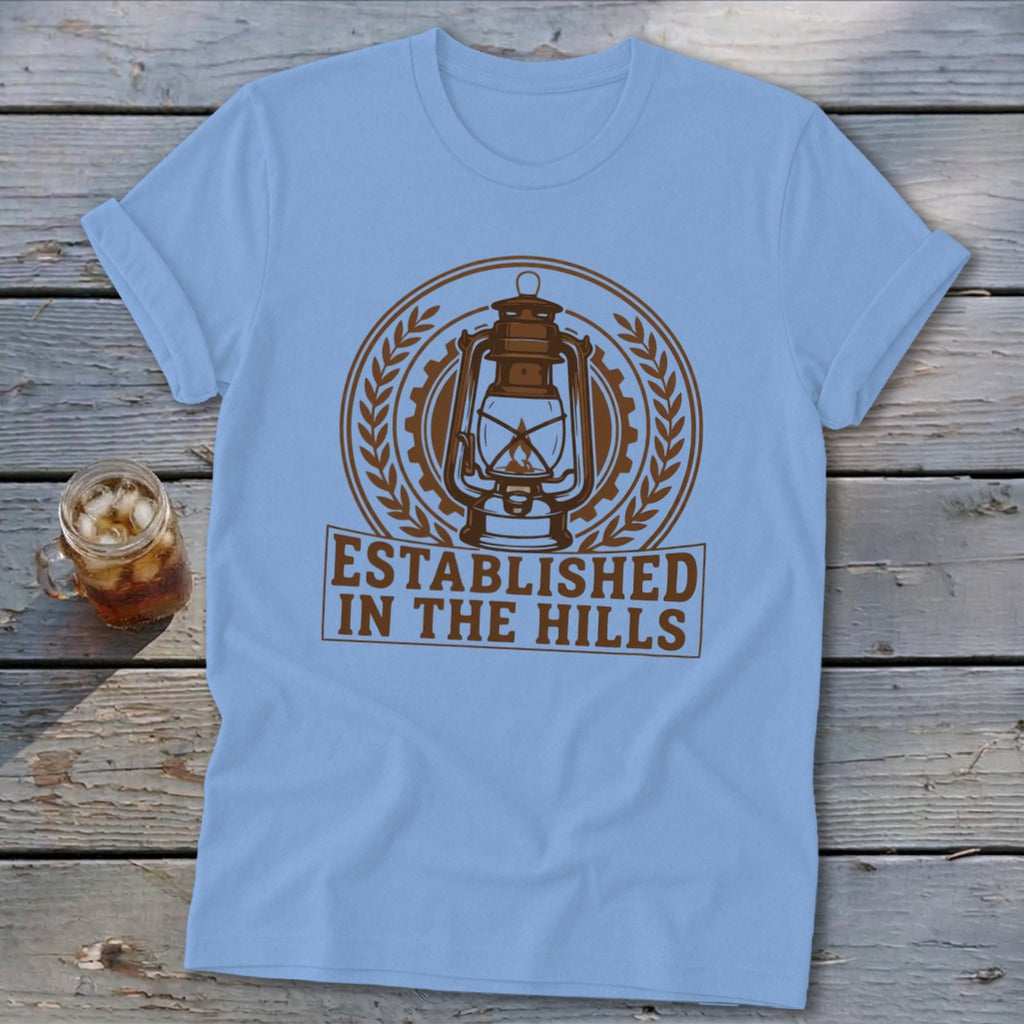 Light blue t-shirt with a vintage lantern design and "ESTABLISHED IN THE HILLS" text.