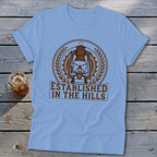 Light blue t-shirt with a vintage lantern design and "ESTABLISHED IN THE HILLS" text.