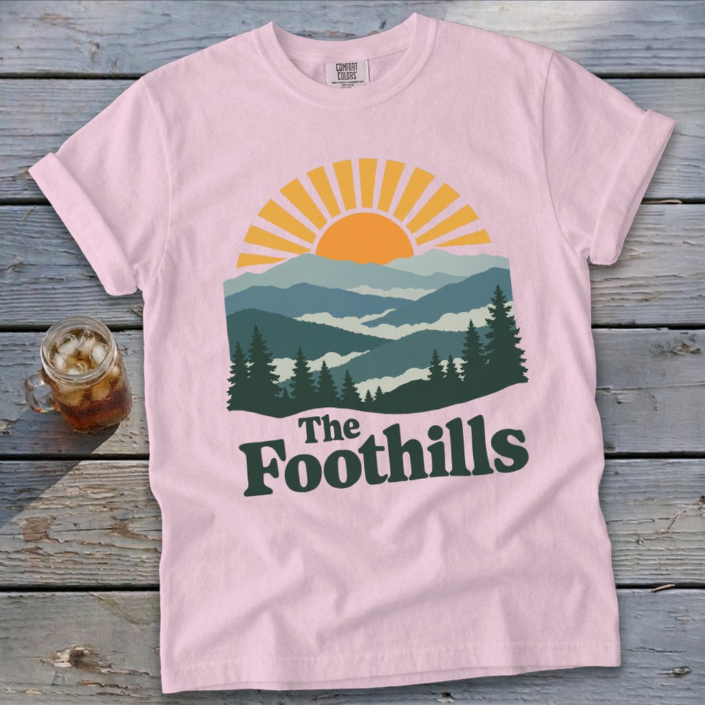 Pink t-shirt with "The Foothills" text and a mountain sunset graphic.