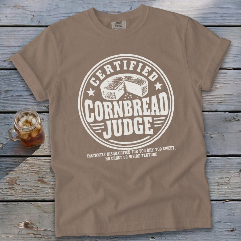 A brown t-shirt featuring a circular white graphic with the text "Certified Cornbread Judge."