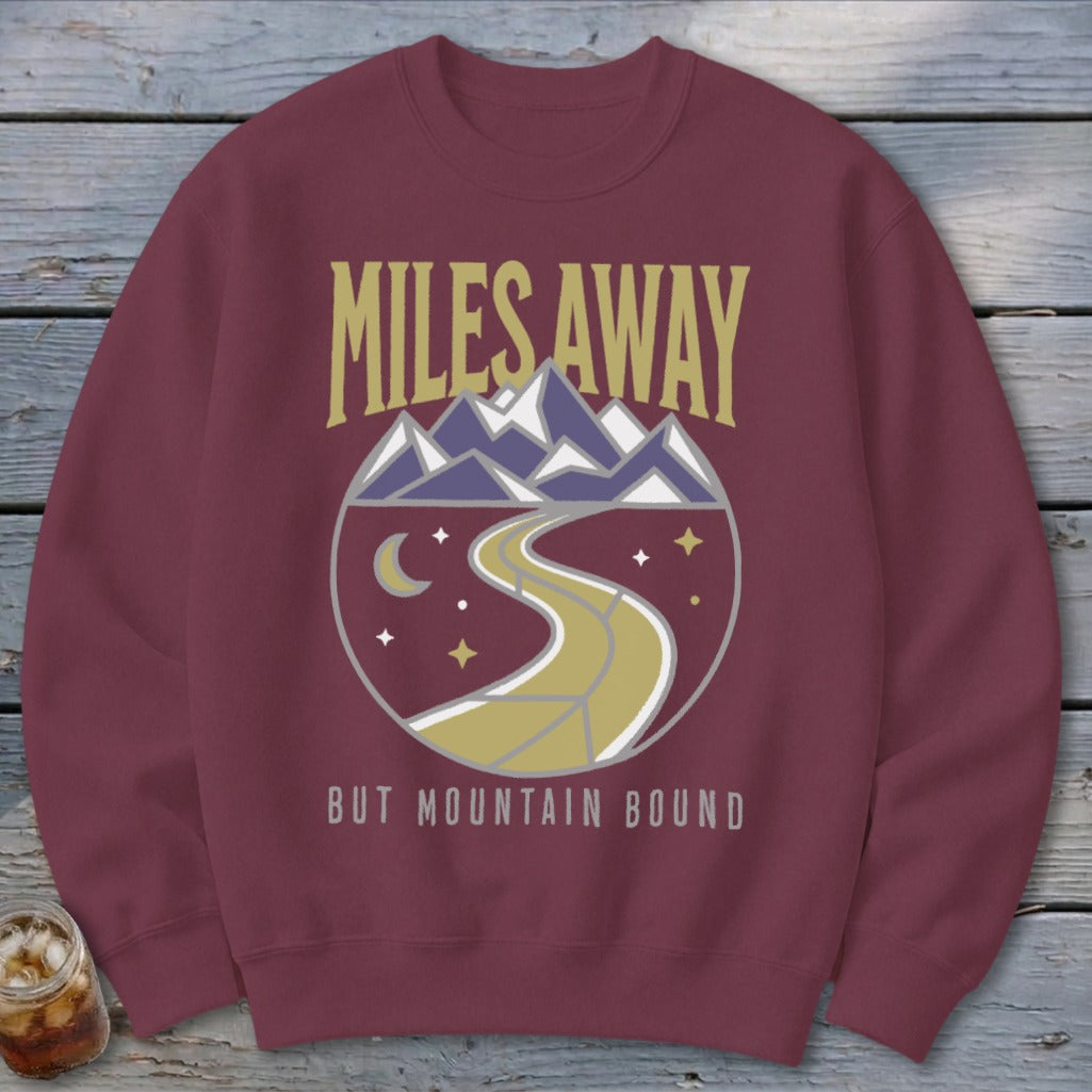 Maroon sweatshirt with "Miles Away But Mountain Bound" text and mountain graphic.
