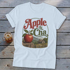 A white t-shirt featuring a retro graphic of an apple, mountains, and cabin with text.