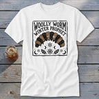 A white t-shirt featuring a black and brown graphic of a woolly worm with the text Woolly Worm Winter Prophet.