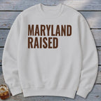 White sweatshirt with "MARYLAND RAISED" text in brown.