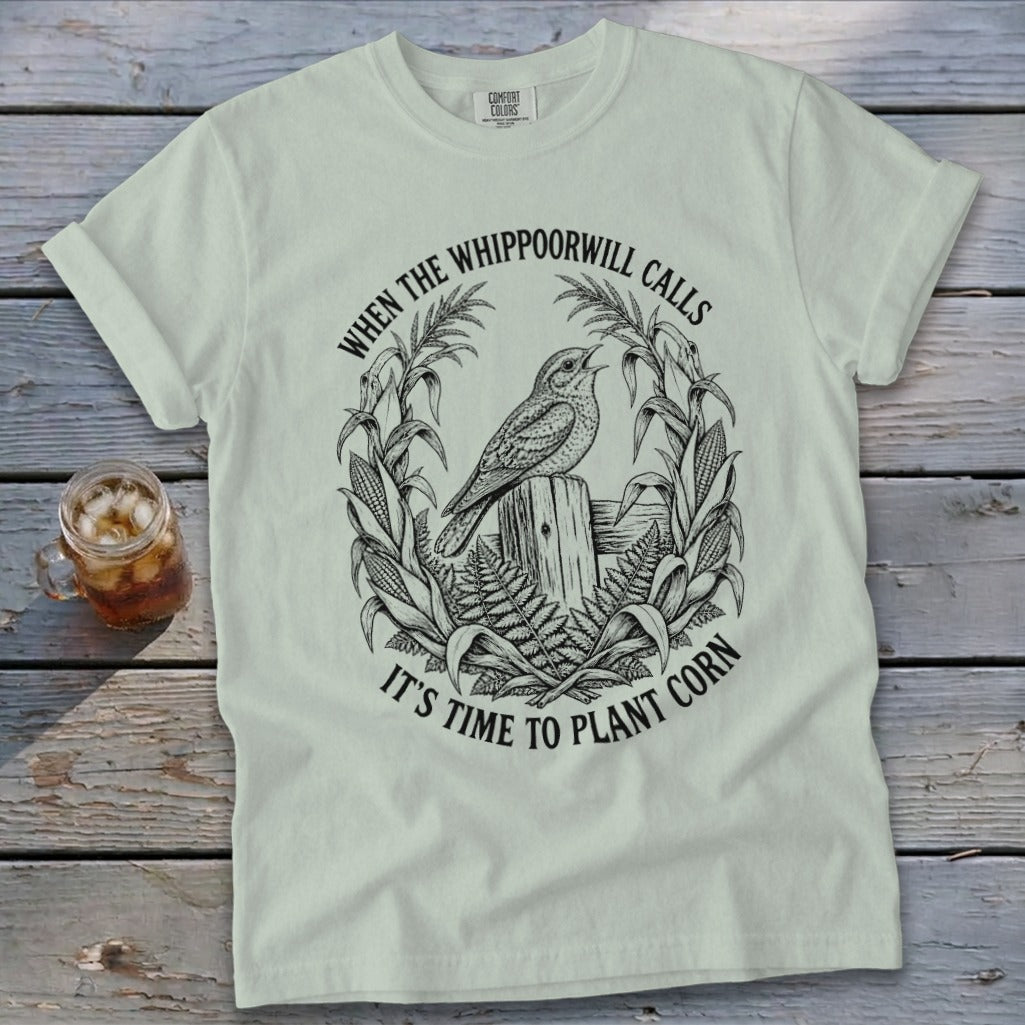 Light green t-shirt with a vintage black line graphic of a bird, corn stalks, and text.