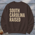Brown crewneck sweatshirt with "South Carolina Raised" printed in tan text.