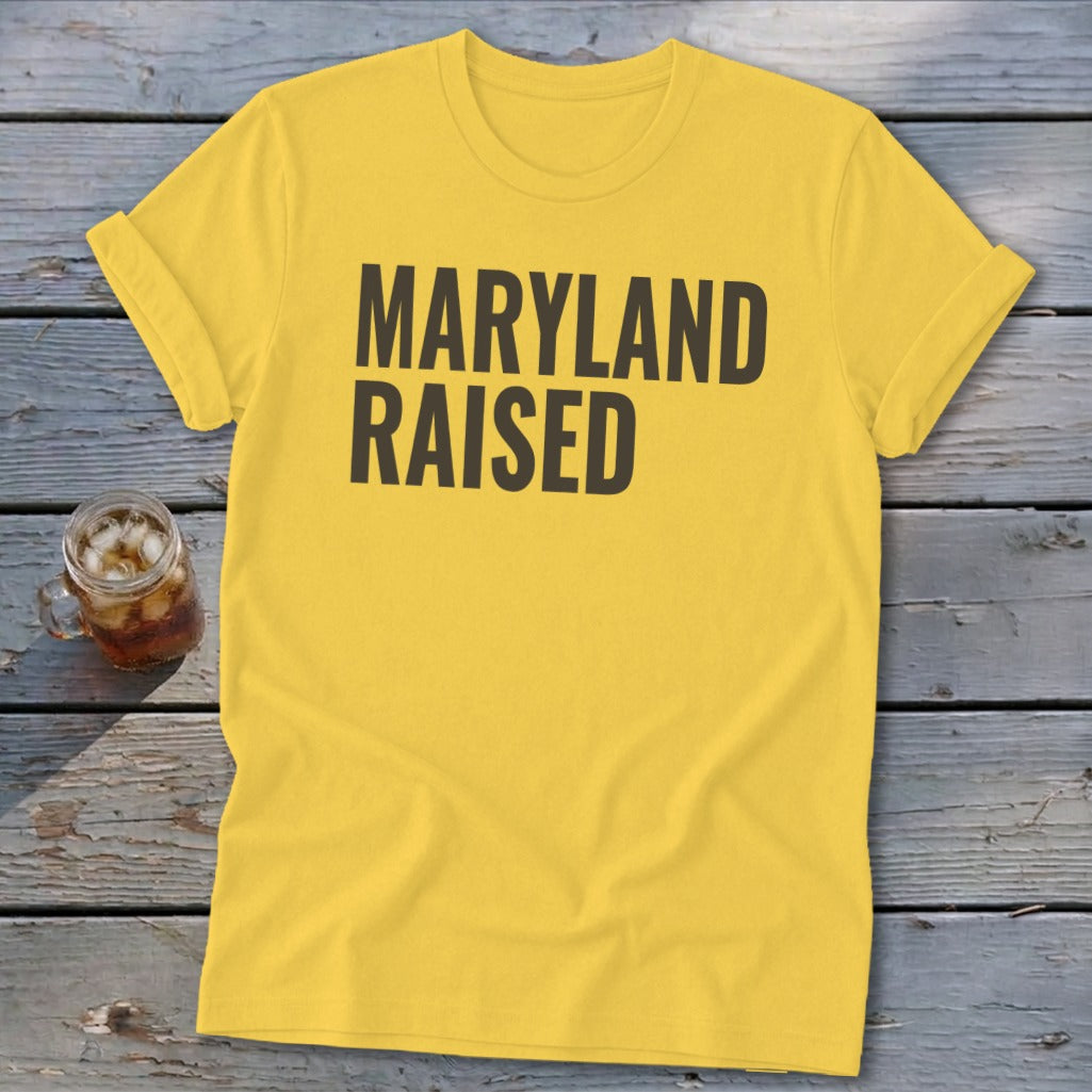 Yellow t-shirt with "MARYLAND RAISED" text in black, beside a glass of iced drink.