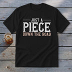Black t-shirt with white text "JUST A PIECE" and pink text "DOWN THE ROAD".