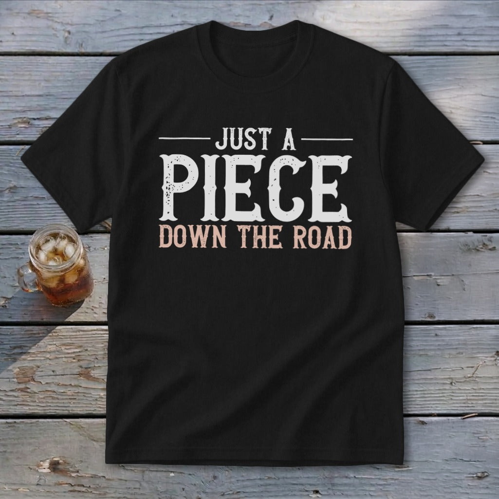 Black t-shirt with white text "JUST A PIECE" and pink text "DOWN THE ROAD".
