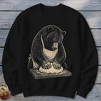 Black sweatshirt with a bear in an apron kneading dough on a wooden board.