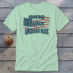 A light green crewneck t-shirt featuring a distressed American flag and text that reads Ohio Raised American Made.