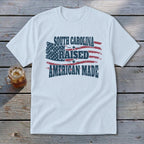 White t-shirt with distressed American flag and text "SOUTH CAROLINA RAISED AMERICAN MADE".