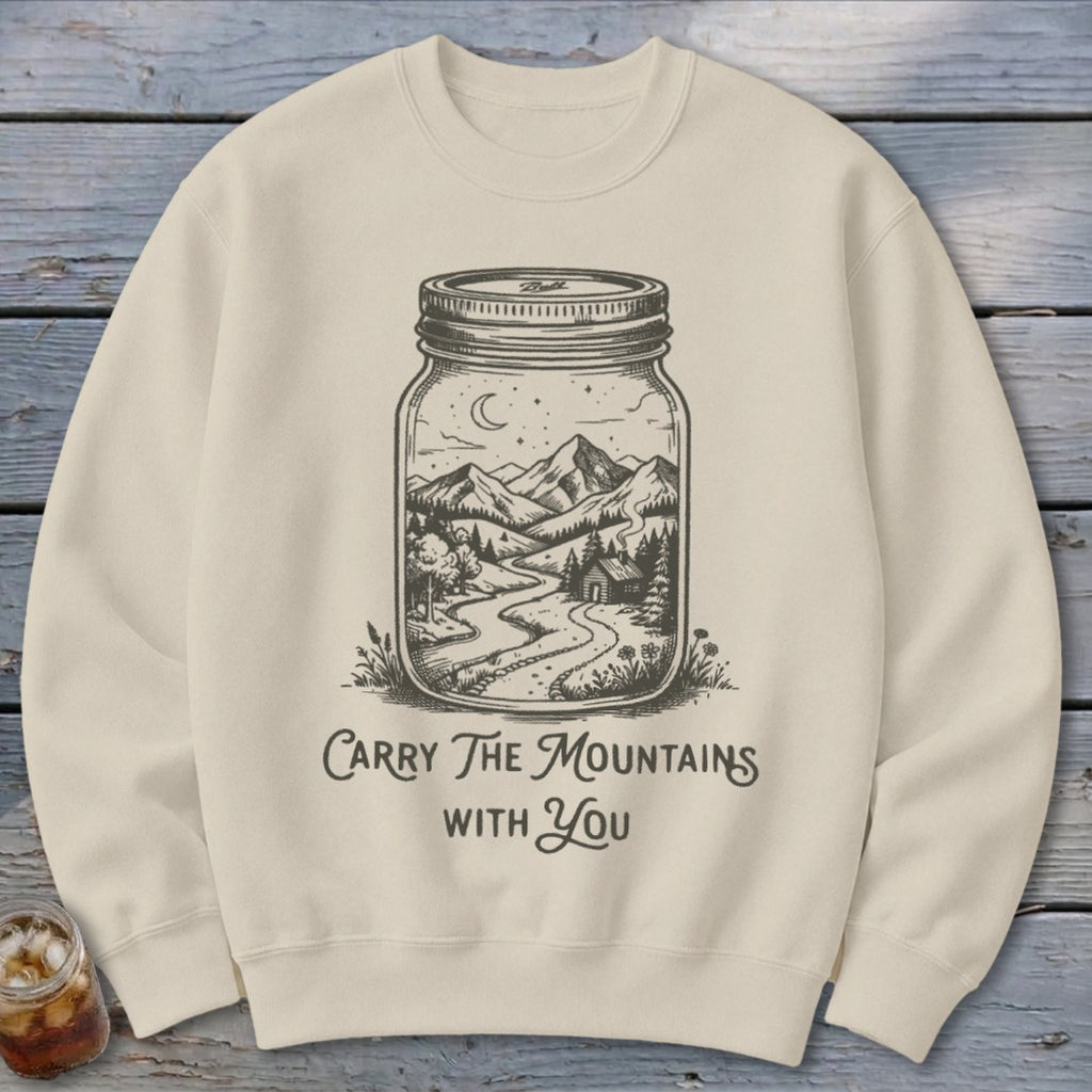 A beige crewneck sweatshirt printed with a mason jar containing a mountain landscape and text reading Carry The Mountains With You.