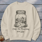 A beige crewneck sweatshirt printed with a mason jar containing a mountain landscape and text reading Carry The Mountains With You.