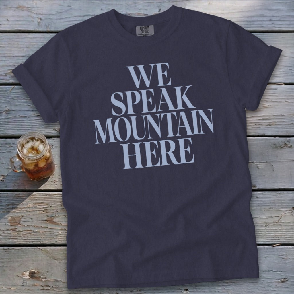 Dark t-shirt with "WE SPEAK MOUNTAIN HERE" text in large white letters.