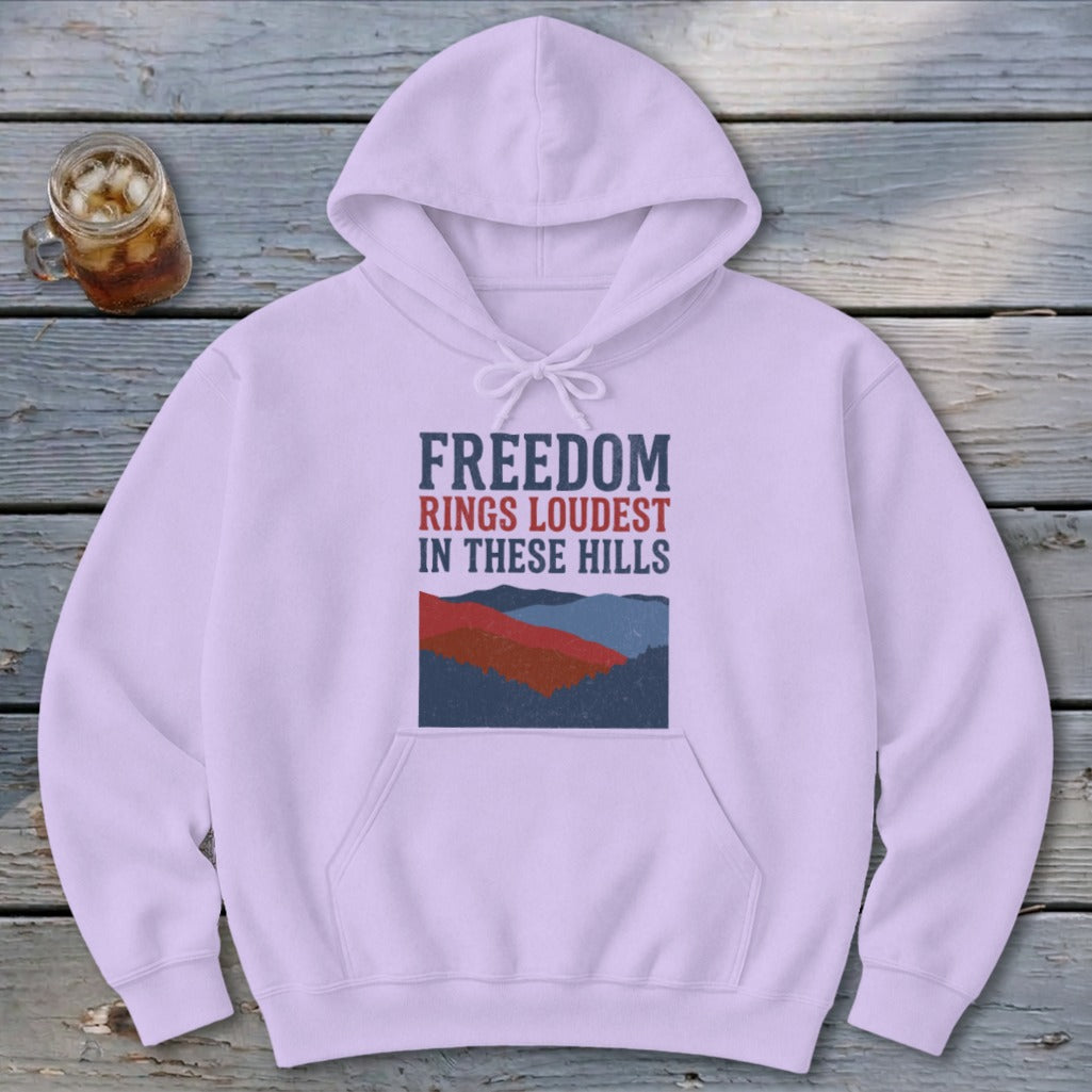 Light purple pullover hoodie with a front graphic displaying mountain scenery and text reading Freedom Rings Loudest in These Hills.