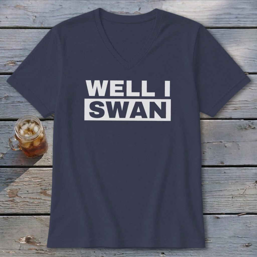 Dark blue v-neck t-shirt with white text reading WELL I SWAN on a wooden background.