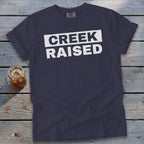 Navy t-shirt with white text reading "CREEK RAISED" across the chest.
